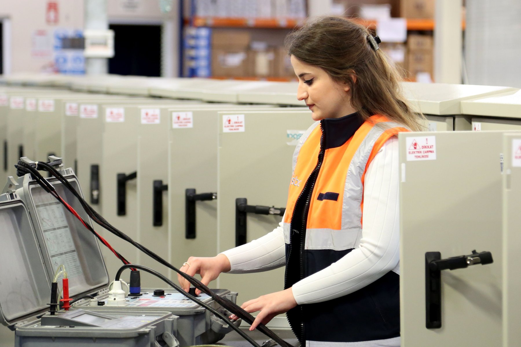 A technician in a high-visibility vest checking electrical cabinets in a workshop