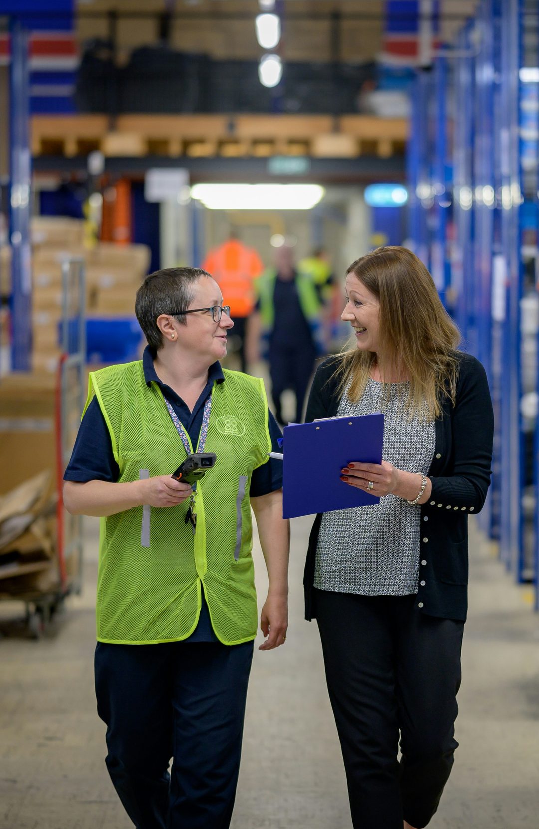 A picker in a yellow vest and a manager talking in a warehouse aisle