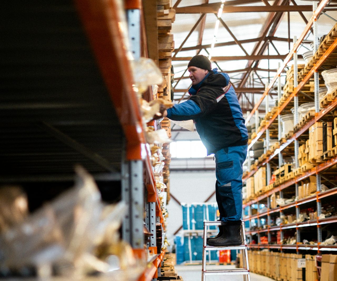 A warehouse worker on a ladder checks the shelving in a warehouse